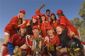 Group of softball players and their coach celebrating a victory with their large trophy at the forefront.